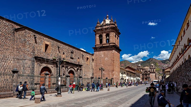 Historic street with impressive bell tower and mountain views, lively with passers-by in clear skies, The churches of Cusco in Peru