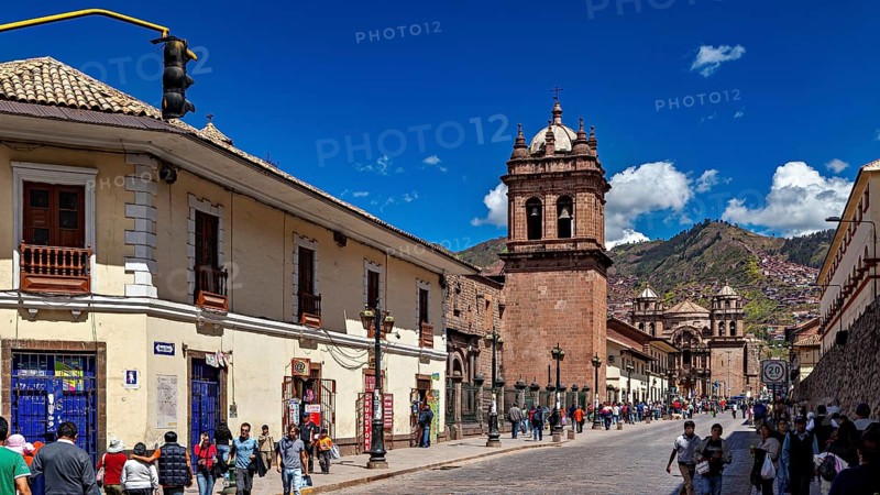 Historic city scene with colonial architecture and busy street life under blue skies, The churches of Cusco in Peru