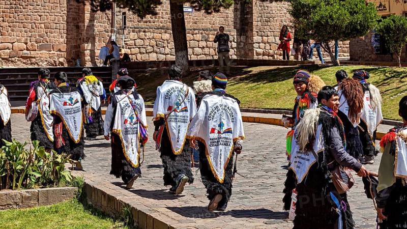 Group of people in white robes with back lettering move down the street during a procession, Traditional parade of festival groups in Cusco in Peru