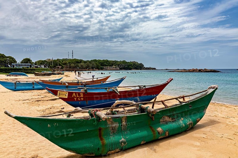 Beach with colorful fishing boats in the sand against a cloudy sky and calm sea, Traditional boats on Trincomalee beach in Sri Lanka