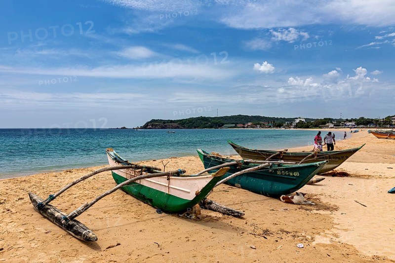 Beach backdrop with green fishing boats in the sand, clear turquoise water and blue sky, traditional boats on Trincomalee beach in Sri Lanka