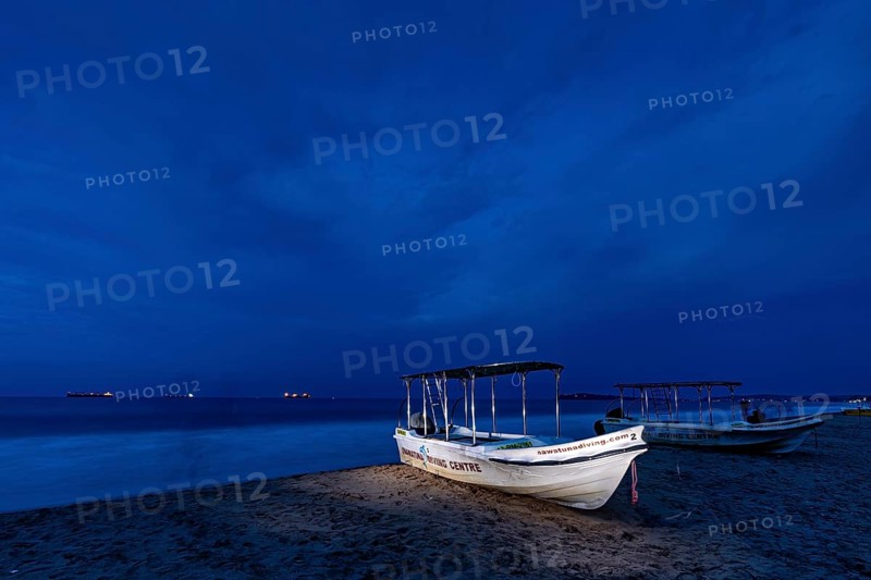 Night landscape with illuminated boat on beach, calm sea and dark sky, traditional boats on Trincomalee beach in Sri Lanka