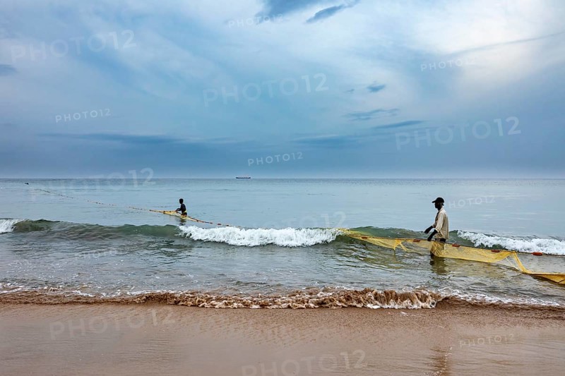 Two fishermen in the sea pull a net across the waves, calm coastal atmosphere, traditional fishermen on Trincomalee beach in Sri Lanka