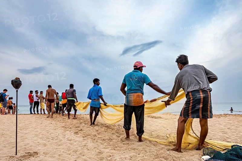 Group of people pulling out a fishing net on the beach, collaborative work at the sea, traditional fishermen on Trincomalee beach in Sri Lanka