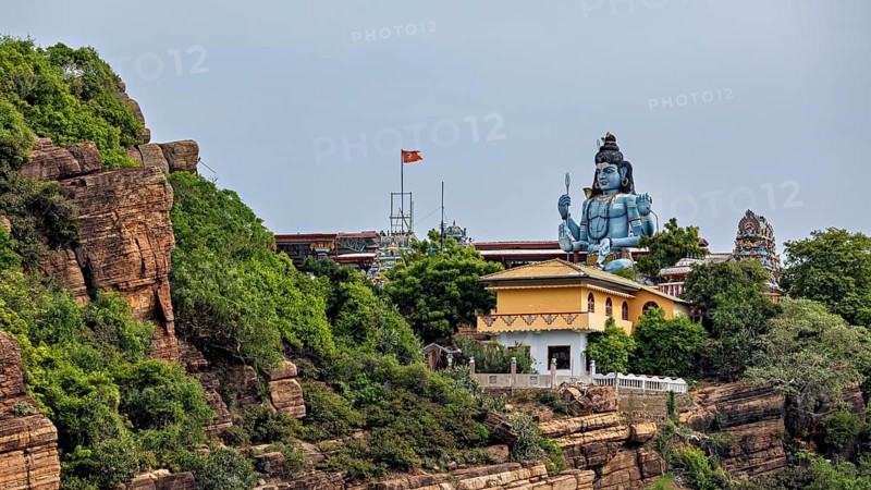 Temple and large Shiva statue on rocky hill surrounded by green vegetation, Koneswaram temple in Trincomalee in Sri Lanka