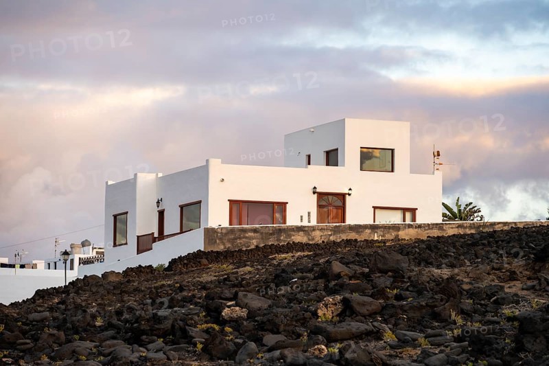 Black coast of volcanic rocks behind typical white houses of the village of La Santa, at sunset, Lanzarote, Canary Islands, Spain
