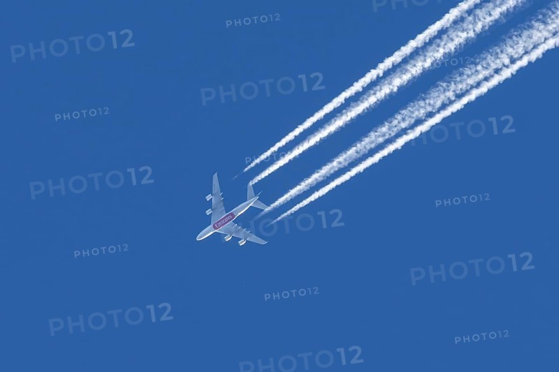 Airbus A380 jet passenger aircraft of Emirates airlines flying in a blue sky with contrails or vapour trails behind, England, United Kingdom