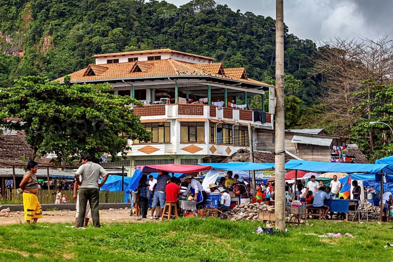 Large house in the background of a busy market square with people and mountains in the distance, The Rurrenabaque market in the Amazon jungle rainforest in Bolivia