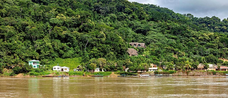 A forest next to a river with houses scattered along the shore under a cloudy sky, the city of Rurrenabaque in the Amazon jungle rainforest in Bolivia
