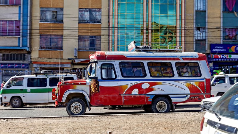 A red and white bus travels through a busy street surrounded by multi-colored buildings, traffic in the city of La Paz in Bolivia