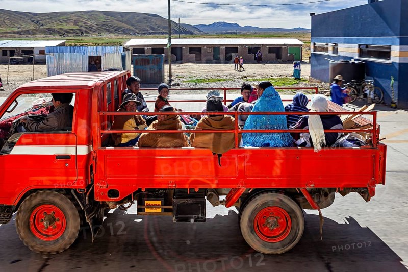A red truck transports several people through a rural area in a quiet atmosphere, Road traffic in the city of La Paz in Bolivia
