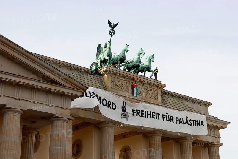 Several activists drop a banner with the inscription Never again genocide, freedom for Palestine and the Palestinian flag and set off pyrotechnics at the Brandenburg Gate, Berlin, 13.11.2025