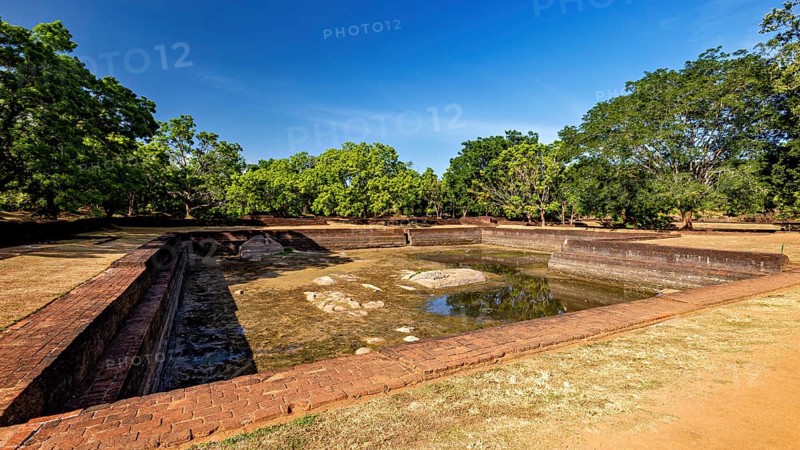 An empty brick water pool in a historic setting with green trees, the temples, dagobas, and pagodas at Lion Rock near Sigiriya in Sri Lanka