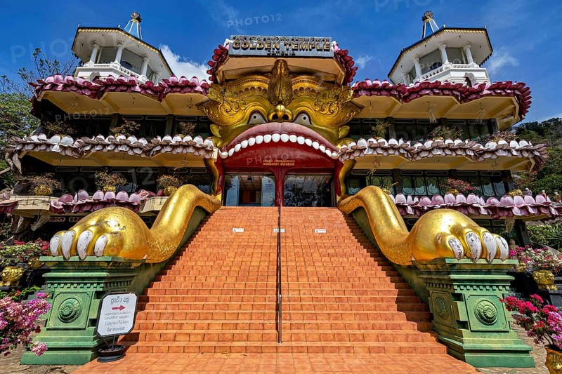 Entrance to a temple with a large golden sculpture and stone stairs decorated with ornaments, The cave temples of Dambulla in Sri Lanka