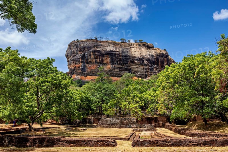 Historic ruins and lush greenery in front of an impressive rock under a blue sky, The Lion Rock near Sigiriya in Sri Lanka