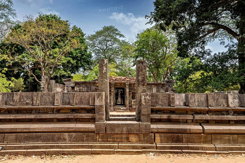 Stone gate marking the entrance to an ancient structure under a clear sky, surrounded by trees, The temples of Polonnaruwa in Sri Lanka