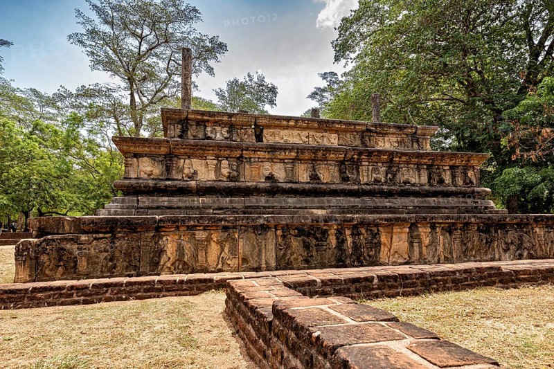 Engraved stone tablet with historical relics under a cloudy sky surrounded by trees, The temples of Polonnaruwa in Sri Lanka