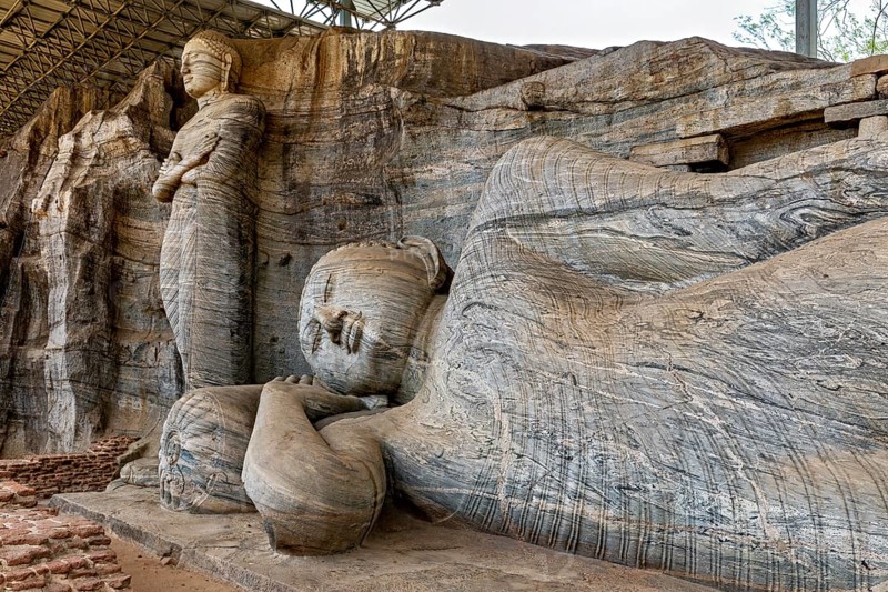 Close-up of the artistic detail of a large reclining Buddha statue next to a standing figure carved out of rocks, The Buddhas at Polonnaruwa in Sri Lanka