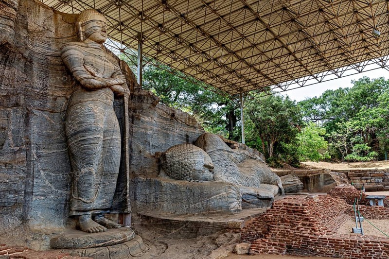 Monumental rock statue with standing and resting figure under a canopy surrounded by nature and brick walls, The Buddhas near Polonnaruwa in Sri Lanka