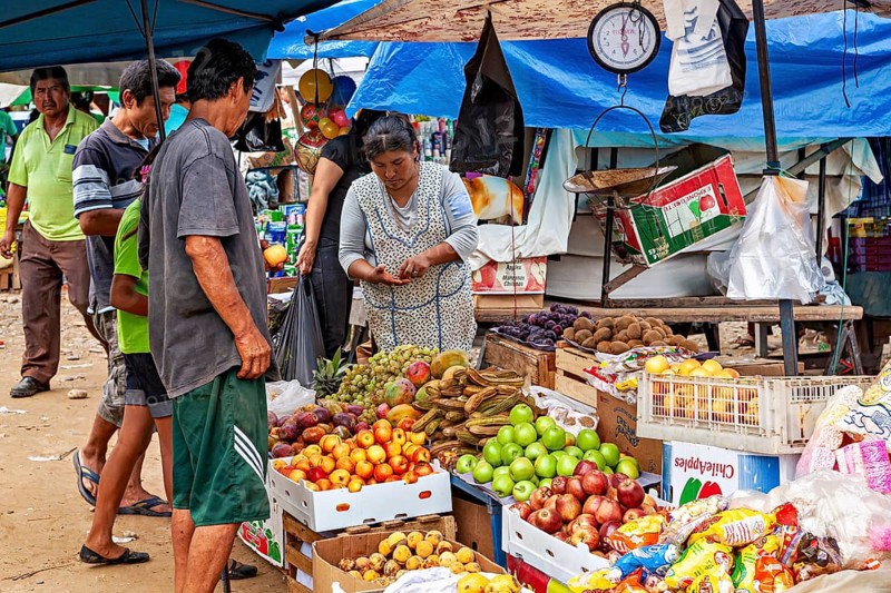 Fruit and vegetables in boxes at a market stand where customers look around and shop, The Rurrenabaque market in Bolivia