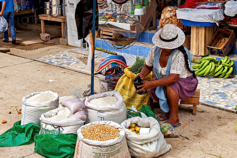 Woman wearing a hat sitting at the market and opening a bag of grain, The Rurrenabaque market in Bolivia