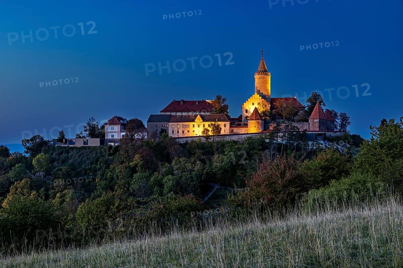 A castle on a wooded hill, illuminated at dusk with dark skies, The Leuchtenburg near Kahla im Saale Holzlandkreis in Thuringia