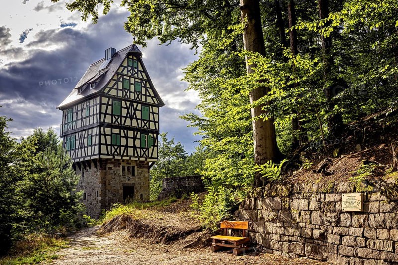Half-timbered house in the forest, next to a paved path and a wooden bench, under sunlight with partly cloudy sky, The Herzogstuhl in the Saale Holzlandkreis district in Thuringia