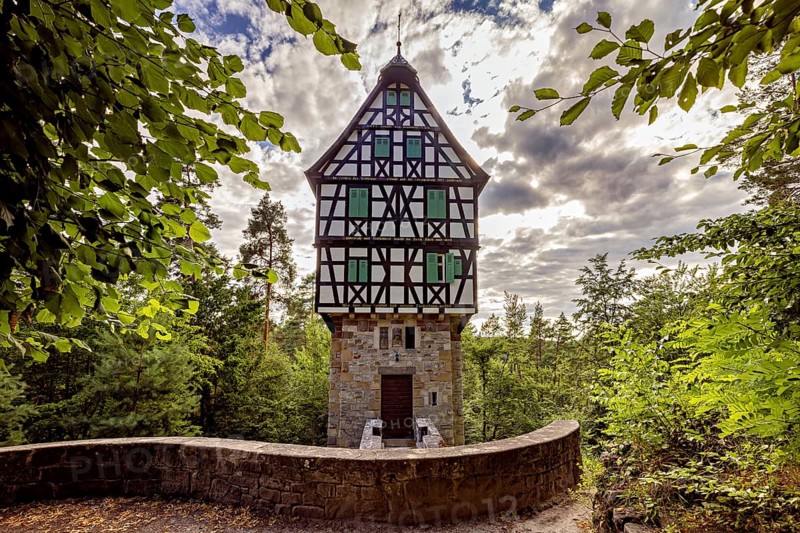 Half-timbered house in the forest surrounded by leaves, under a cloudy sky, with a curved stone wall in the foreground, The Herzogstuhl in the Saale Holzlandkreis district in Thuringia