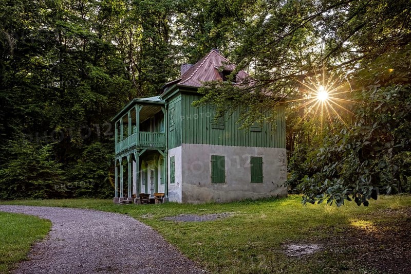 Green house in the forest with evening sun, quiet path and wooden veranda in peaceful surroundings, The Riesenecke hunting complex in the Saale Holzland district in Thuringia