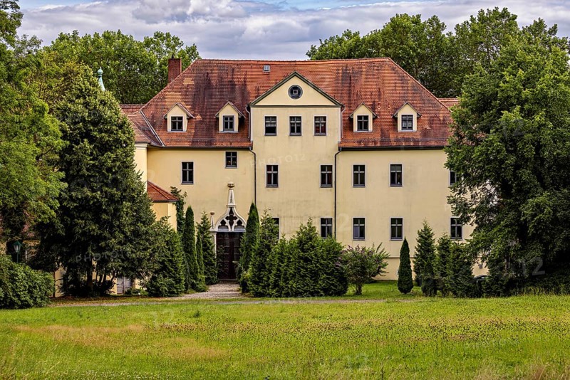 Yellow castle with distinctive roof and well-kept garden surrounded by trees, The Hummelshain hunting lodge in Thuringia