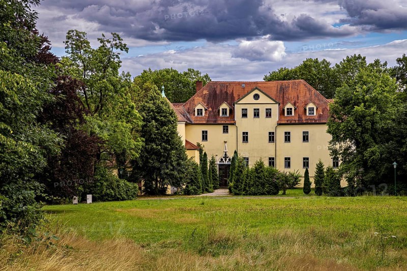 Manor house surrounded by green trees and meadows, under a cloudy sky, The Hummelshain hunting lodge in Thuringia