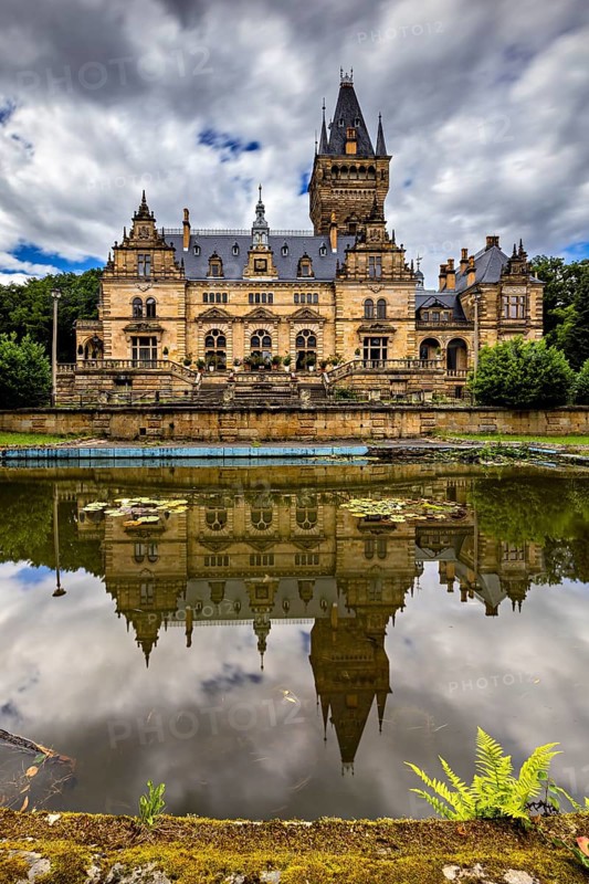 Magnificent castle with mirror lake and dramatic sky in the background, Hummelshain hunting lodge in Thuringia