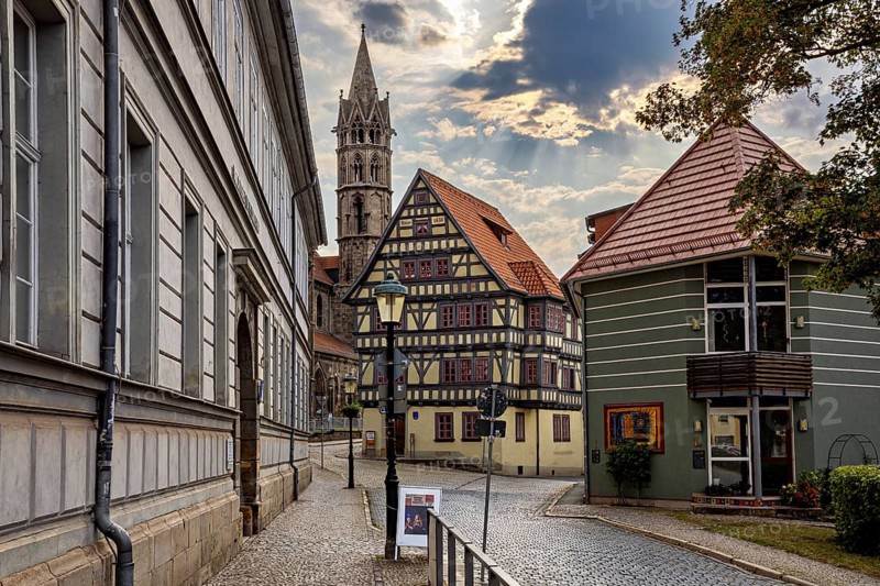 Paved street with half-timbered houses and church tower under a cloudy sky, the old town of Arnstadt in Thuringia