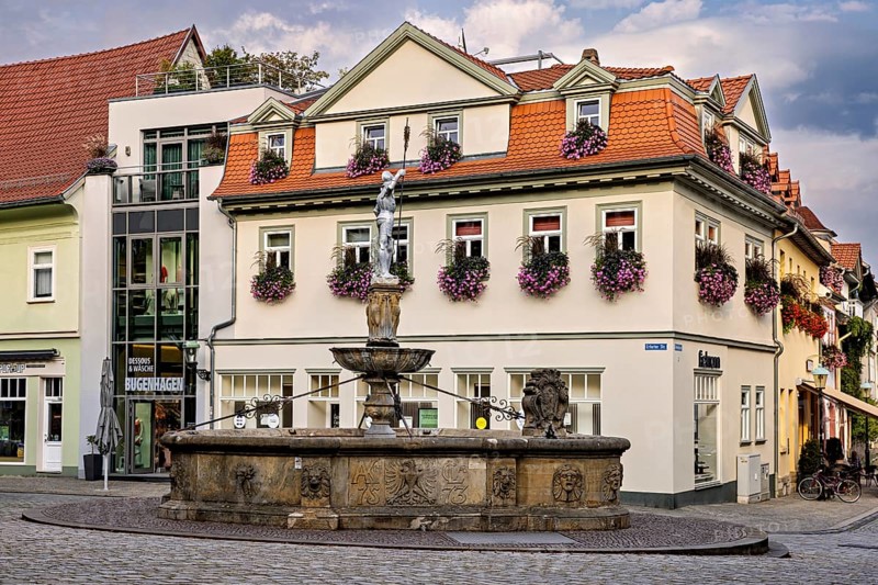A fountain in front of a house decorated with flowers under a sunny sky, the old town of Arnstadt in Thuringia