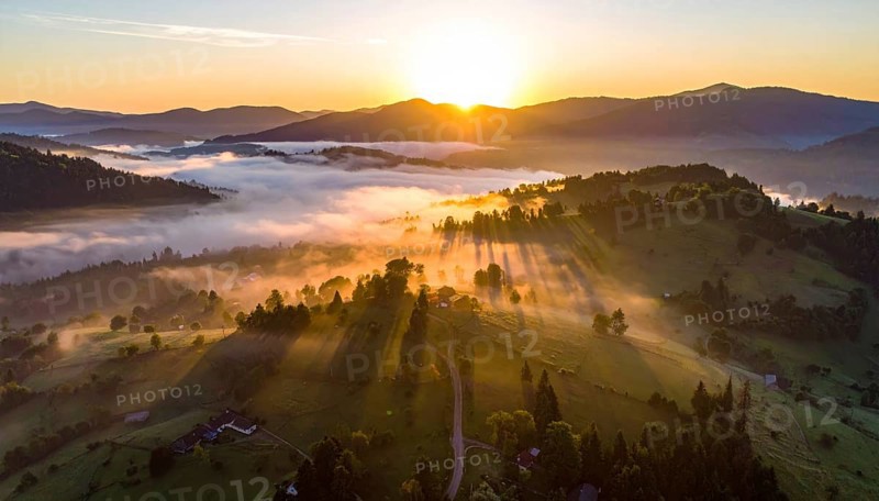 Sunrise over a fog covered village in a rural landscape, golden morning light, serene autumn atmosphere, hills and mountains in the background, AI generated