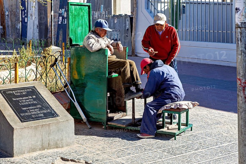 Three men interact in a relaxed street scene at a shoe shiner in the old town, show shiners in the town of Uyuni in the Salar de Uyuni in Bolivia