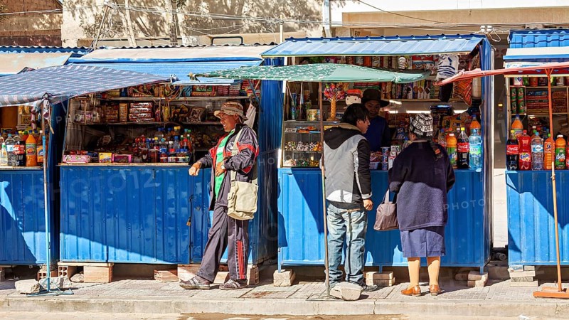 Street market with a blue stall, people buy colourful bottles and products under a blue sky, small shops in the town of Uyuni in the Salar de Uyuni in Bolivia