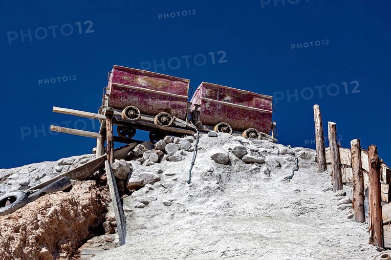 Two old mine cars standing on a rocky structure above a stony slope under a clear sky, mining lore at the Cerro Rico silver mountain near Potosi Bolivia