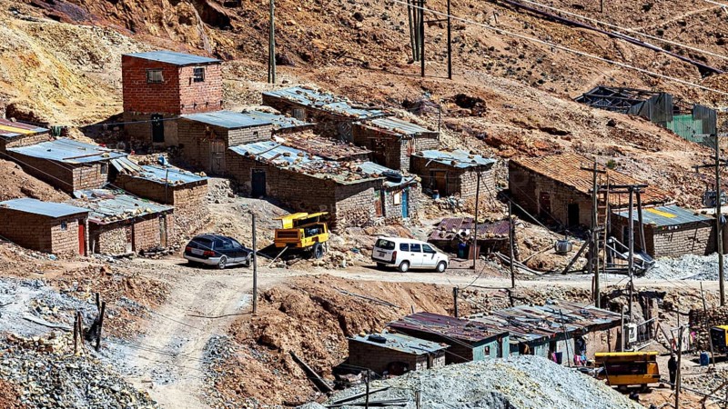 Several clay-coloured houses in a mountainous landscape with parked cars and rubble, The silver mines of Potosi Bolivia