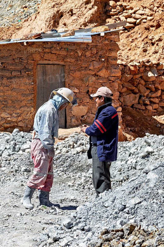 Two men in work clothes talk in a dusty mining landscape, The miners of the Cerro Rico silver mountain near Potosi Bolivia