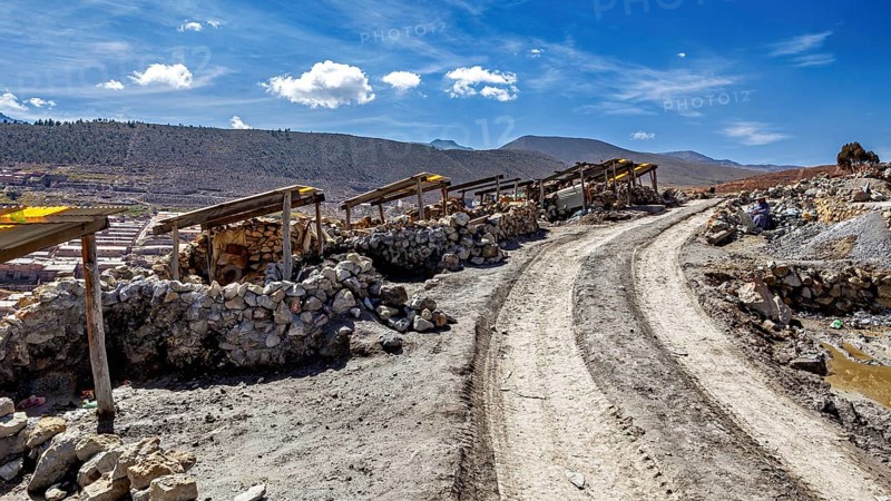 Dusty path with piles of stones next to a mountainous landscape under a blue sky with clouds, The silver mines of Potosi Bolivia