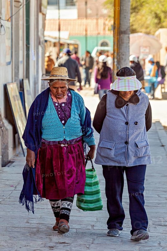 Two woman in traditional dress walk along a sunny street, people of the town of Uyuni in the Salar de Uyuni in Bolivia