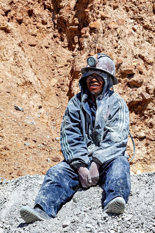 A miner in dusty clothing sits in front of a rock face near a mine, The miners of the Cerro Rico silver mountain near Potosi Bolivia