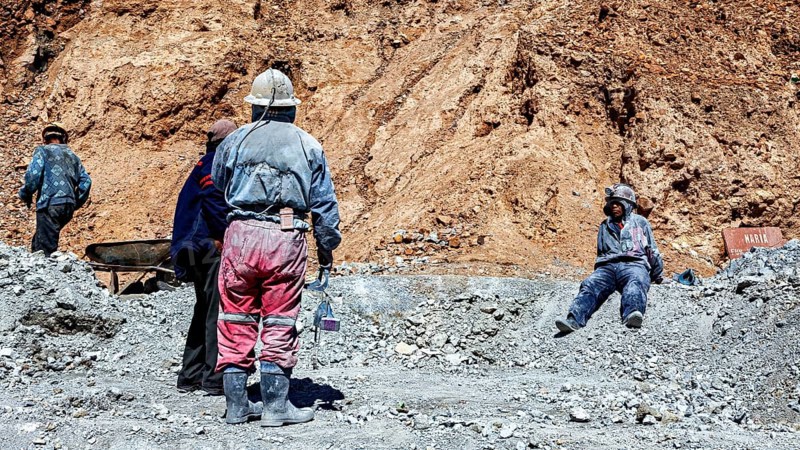 Miners in different clothes stand or sit in a barren, dusty environment, The miners of the Cerro Rico silver mountain near Potosi Bolivia