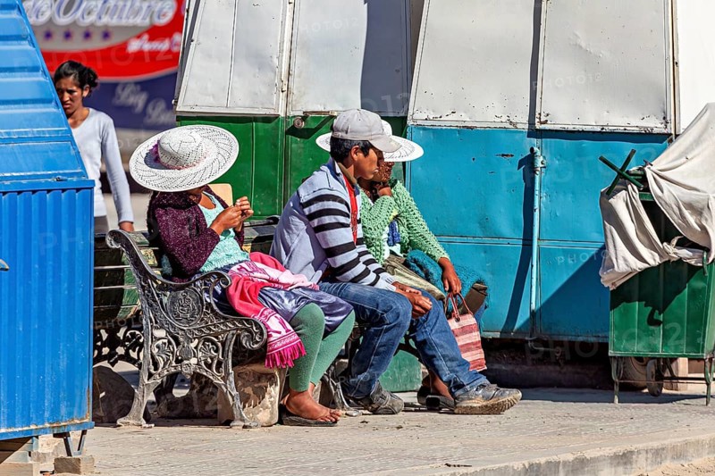 People with hats sitting on a bench in the sun at a market stall, people of the city of Uyuni in the Salar de Uyuni in Bolivia