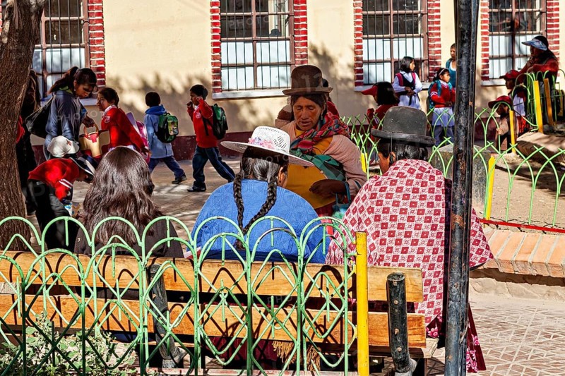 Women in traditional dress sit in the park while children play, people of the town of Uyuni in the Salar de Uyuni in Bolivia
