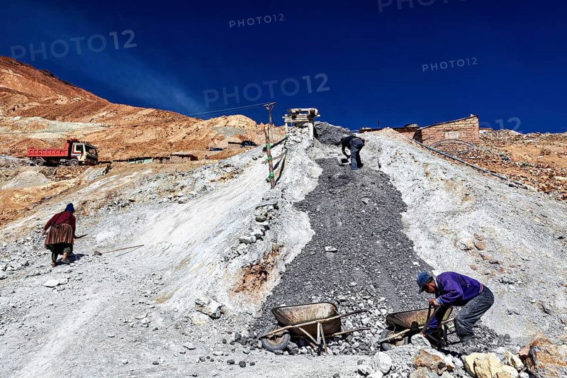 Workers with wheelbarrows on a stony slope under a bright blue sky, The silver mines of Potosi Bolivia