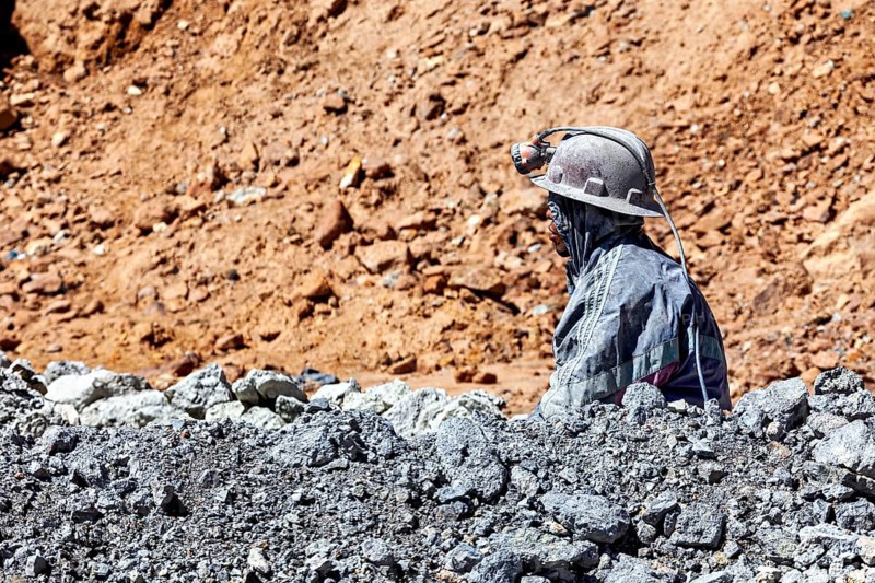 A miner gazes into the distance, surrounded by rocks and dusty terrain, The miners of the Cerro Rico silver mountain near Potosi Bolivia