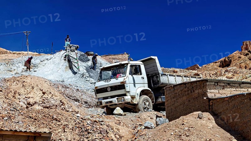 A lorry unloads gravel at a construction site in a mountainous desert landscape under a clear sky, The silver mines of Potosi Bolivia