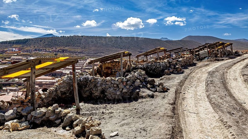 A dirt track leads through a dry, stony landscape under a blue sky with clouds, The silver mines of Potosi Bolivia